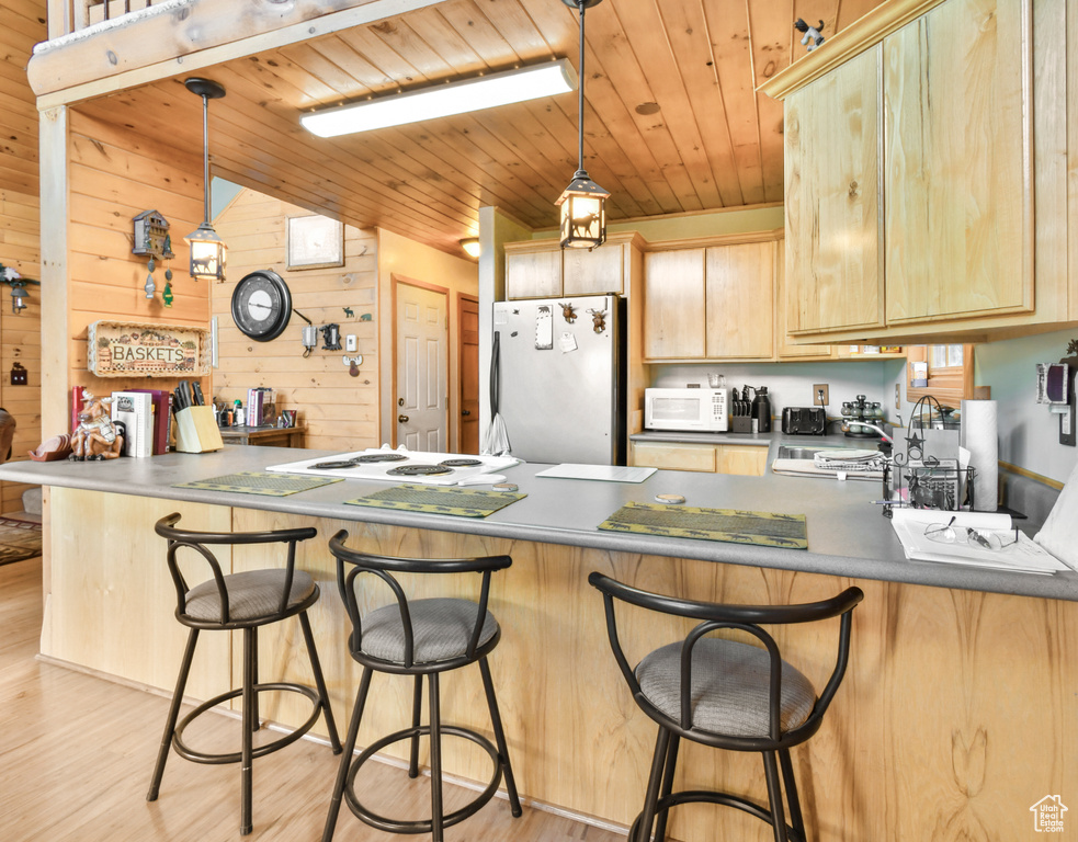 Kitchen with white appliances, light brown cabinetry, a peninsula, light wood-type flooring, and wood walls