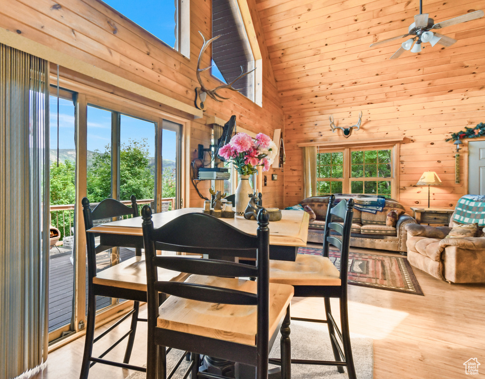 Dining room featuring wooden walls, high vaulted ceiling, wood finished floors, and ceiling fan
