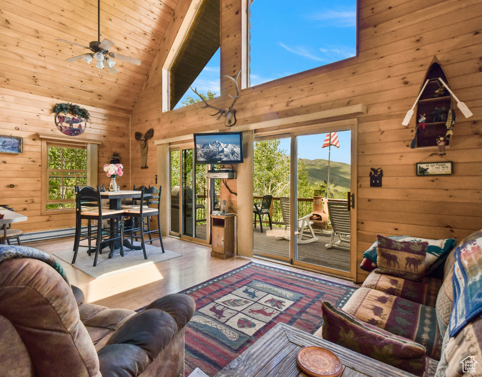 Living room with wood walls, wood finished floors, a ceiling fan, a baseboard radiator, and high vaulted ceiling