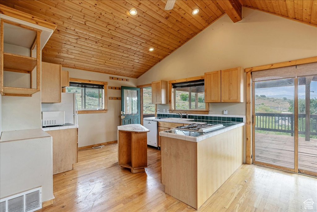 Kitchen featuring white appliances, tile countertops, a peninsula, open shelves, and light wood-style floors