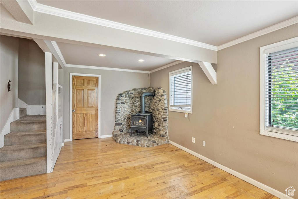 Unfurnished living room featuring a wood stove, plenty of natural light, stairway, wood finished floors, and ornamental molding
