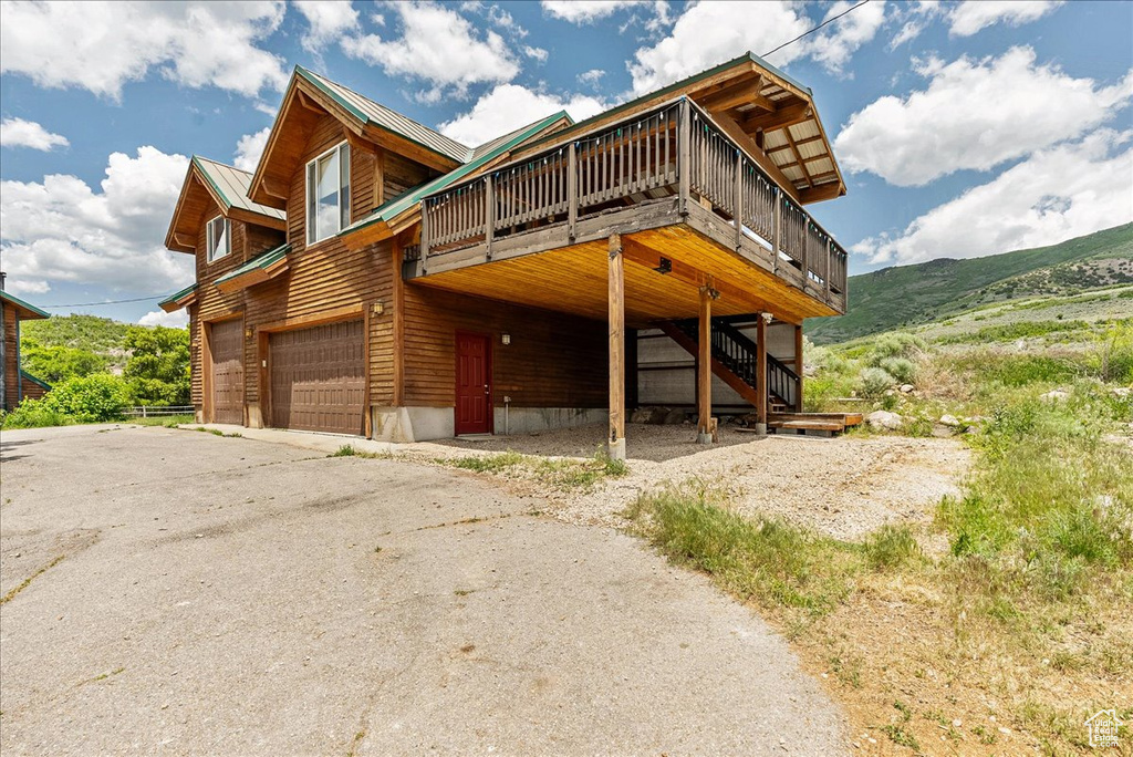 View of front of house featuring a garage, a deck with mountain view, asphalt driveway, stairway, and a metal roof