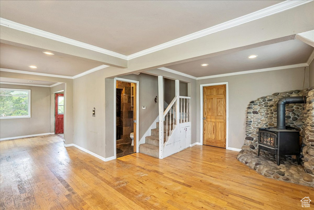 Unfurnished living room featuring light wood-type flooring, stairs, a wood stove, ornamental molding, and recessed lighting