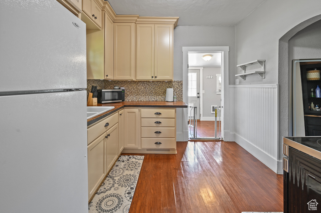 Kitchen with freestanding refrigerator, cream cabinets, wood finished floors, stainless steel microwave, and wainscoting