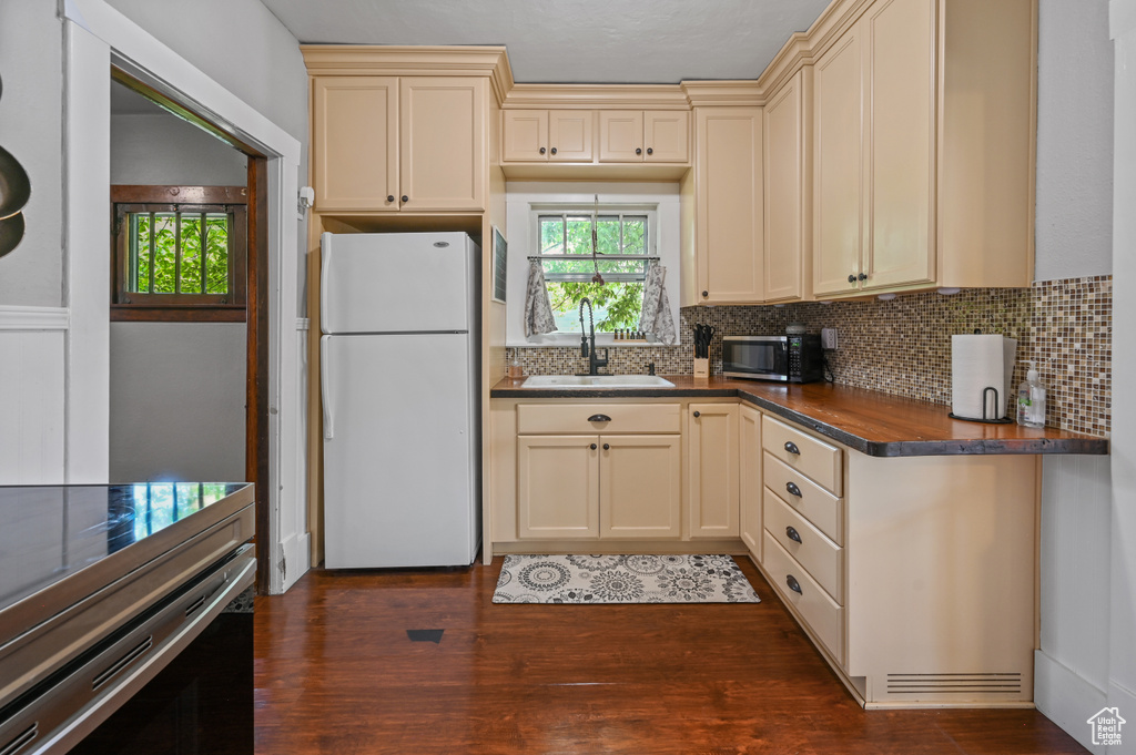 Kitchen featuring freestanding refrigerator, stainless steel microwave, cream cabinets, dark countertops, and tasteful backsplash
