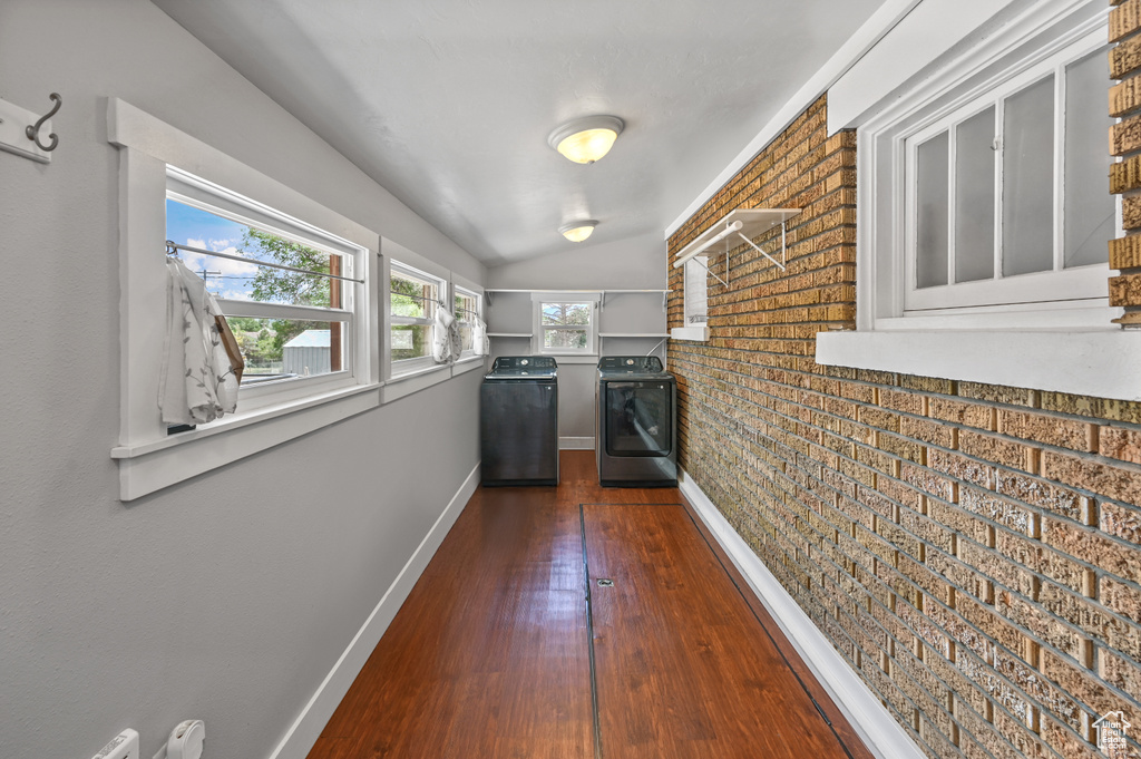 Corridor with washer and dryer, dark wood-type flooring, brick wall, and vaulted ceiling
