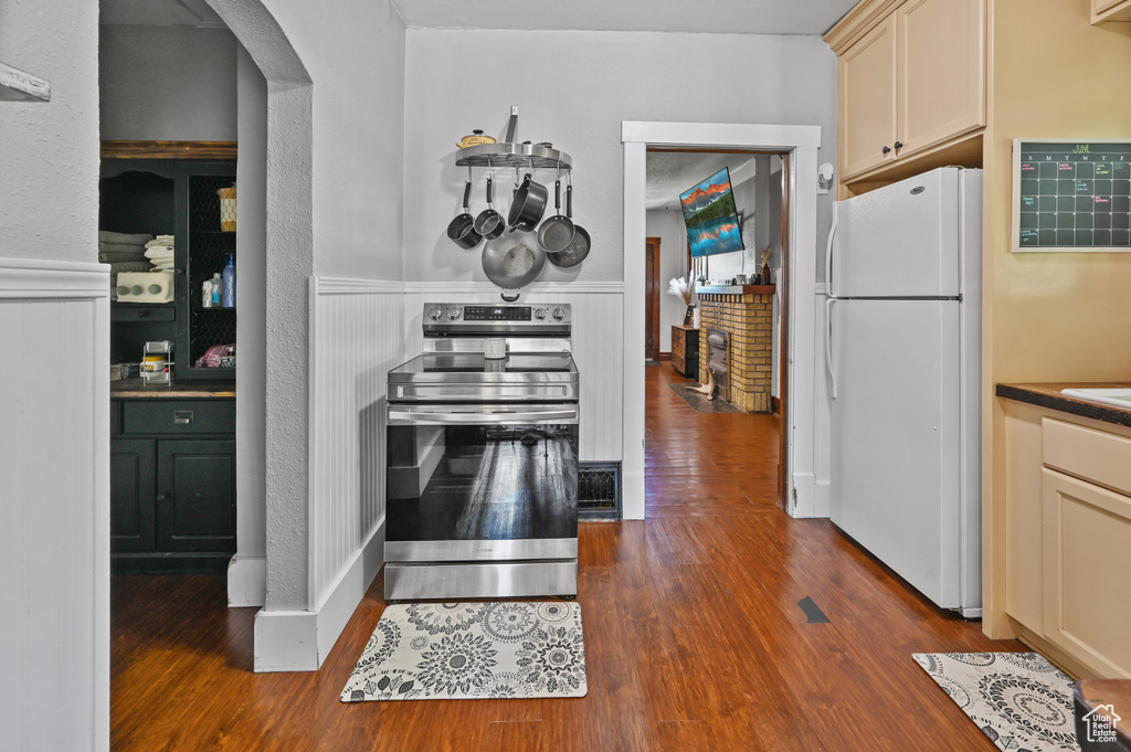 Kitchen with freestanding refrigerator, electric stove, arched walkways, and dark wood-style flooring