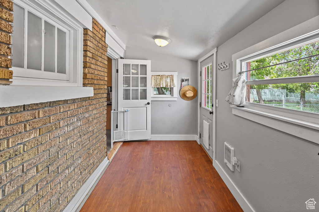 Doorway to outside with dark wood-style floors and brick wall