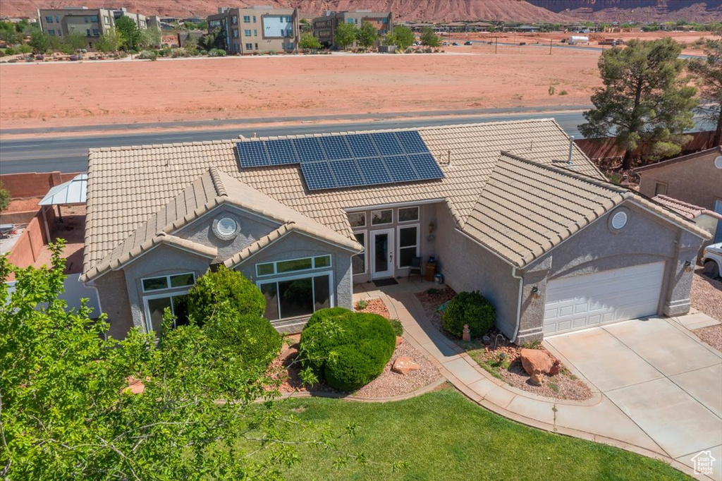 View of front of home with a tiled roof, an attached garage, a mountain view, roof mounted solar panels, and concrete driveway