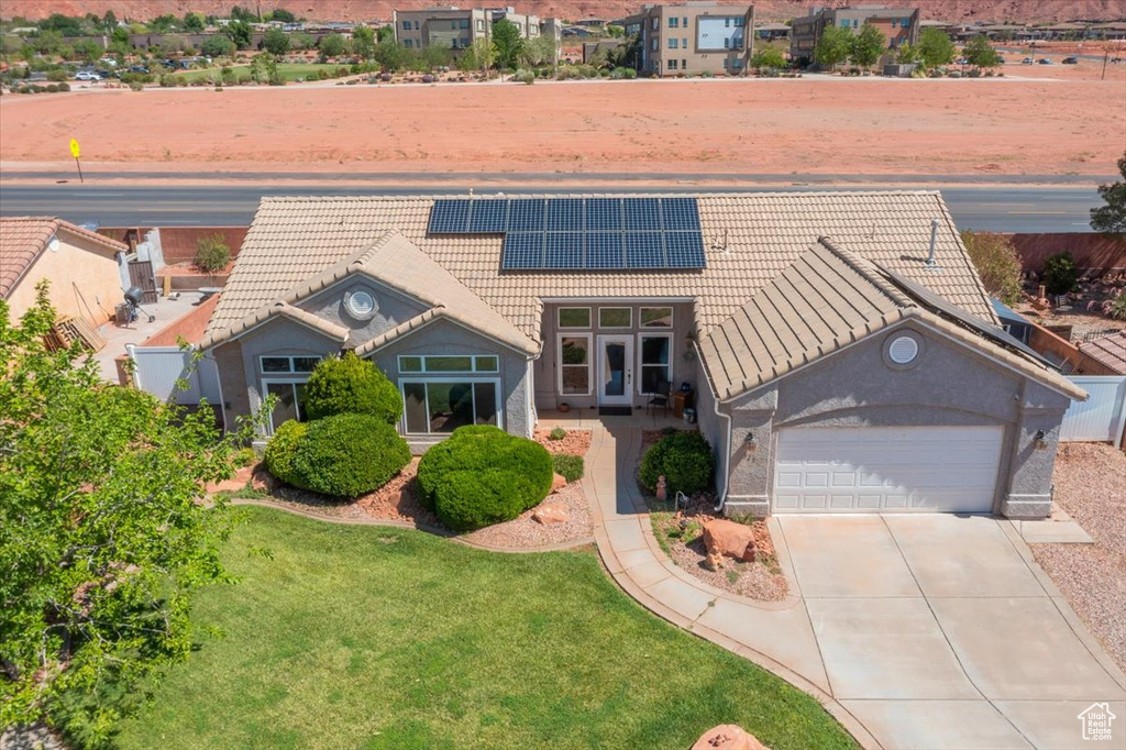 View of front facade featuring a tiled roof, a garage, roof mounted solar panels, driveway, and stucco siding