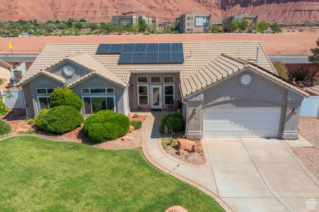 View of front of house featuring a tiled roof, solar panels, driveway, an attached garage, and a front yard