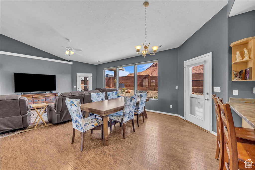 Dining space featuring a chandelier, light wood-style flooring, vaulted ceiling, a ceiling fan, and a textured ceiling