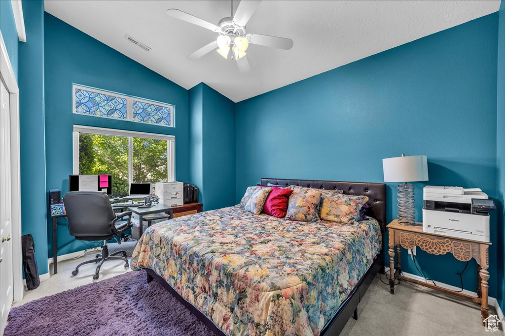 Carpeted bedroom with an office area, ceiling fan, and high vaulted ceiling
