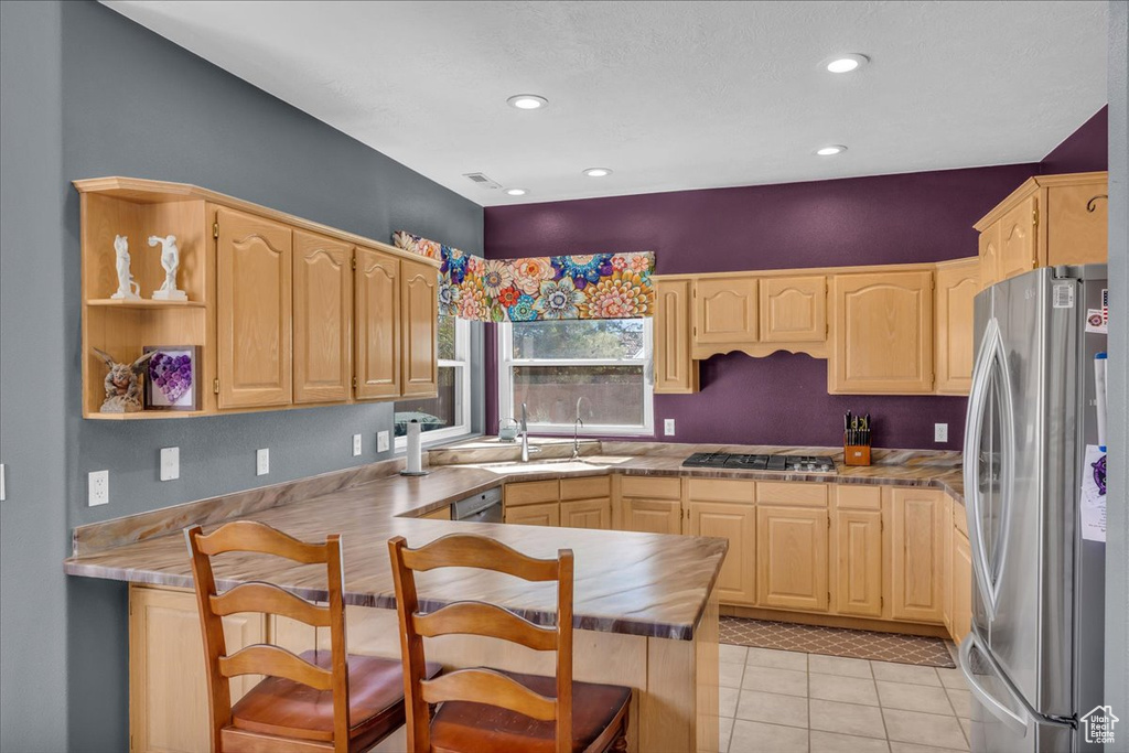 Kitchen with stainless steel appliances, light brown cabinets, a peninsula, light tile patterned floors, and recessed lighting