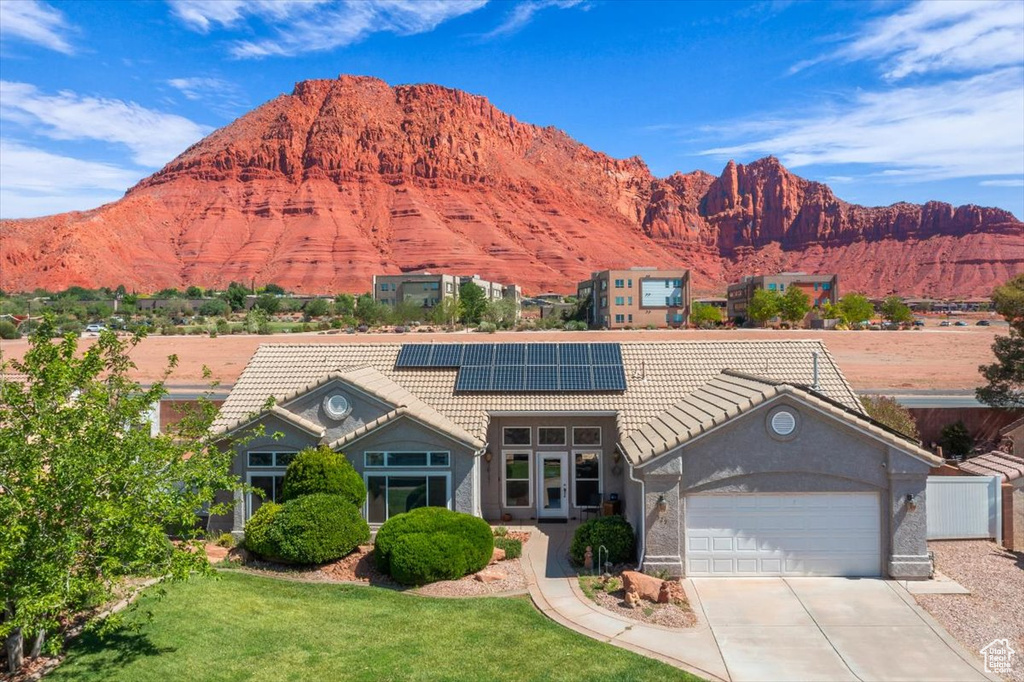 View of front of property with a tile roof, solar panels, a garage, and a mountain view