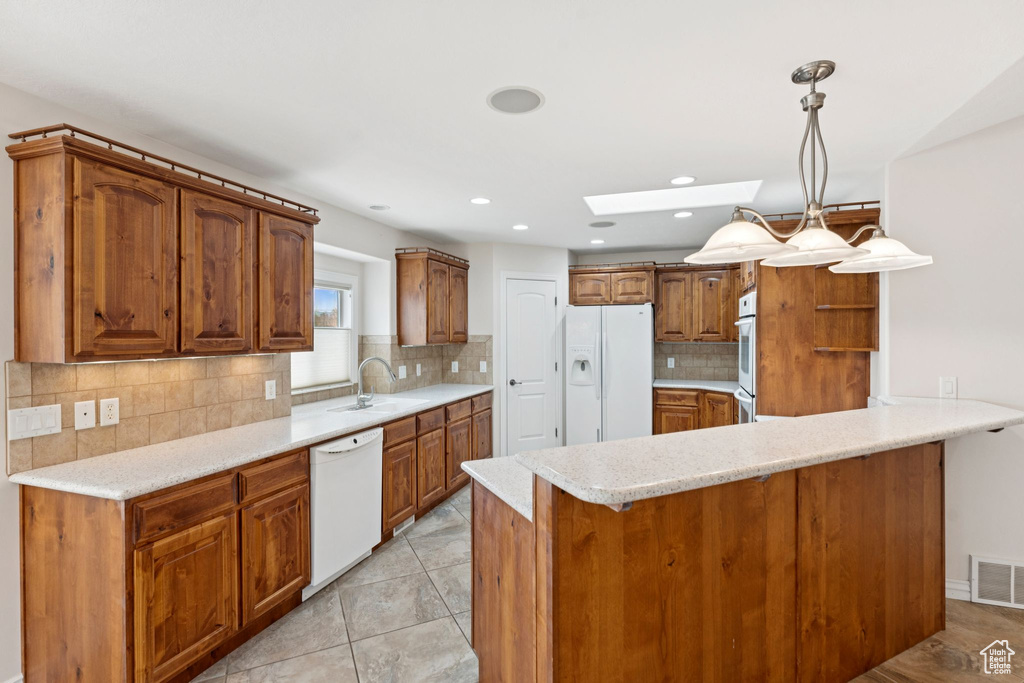 Kitchen with white appliances, a skylight, a peninsula, brown cabinetry, and backsplash