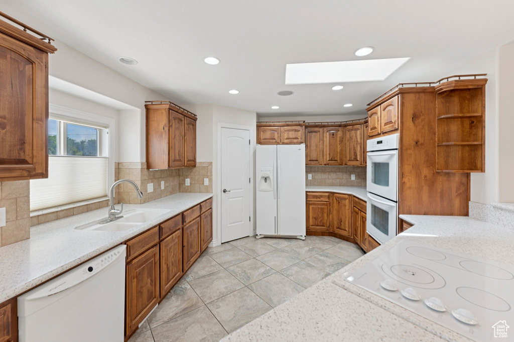 Kitchen featuring white appliances, a skylight, open shelves, backsplash, and brown cabinets