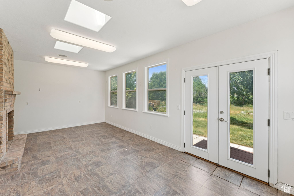 Unfurnished living room with french doors, a skylight, stone finish floors, and a fireplace