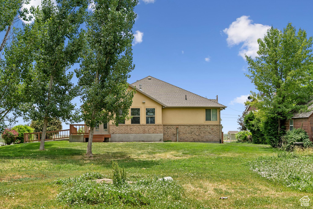 Back of property with a deck, a yard, stucco siding, and brick siding