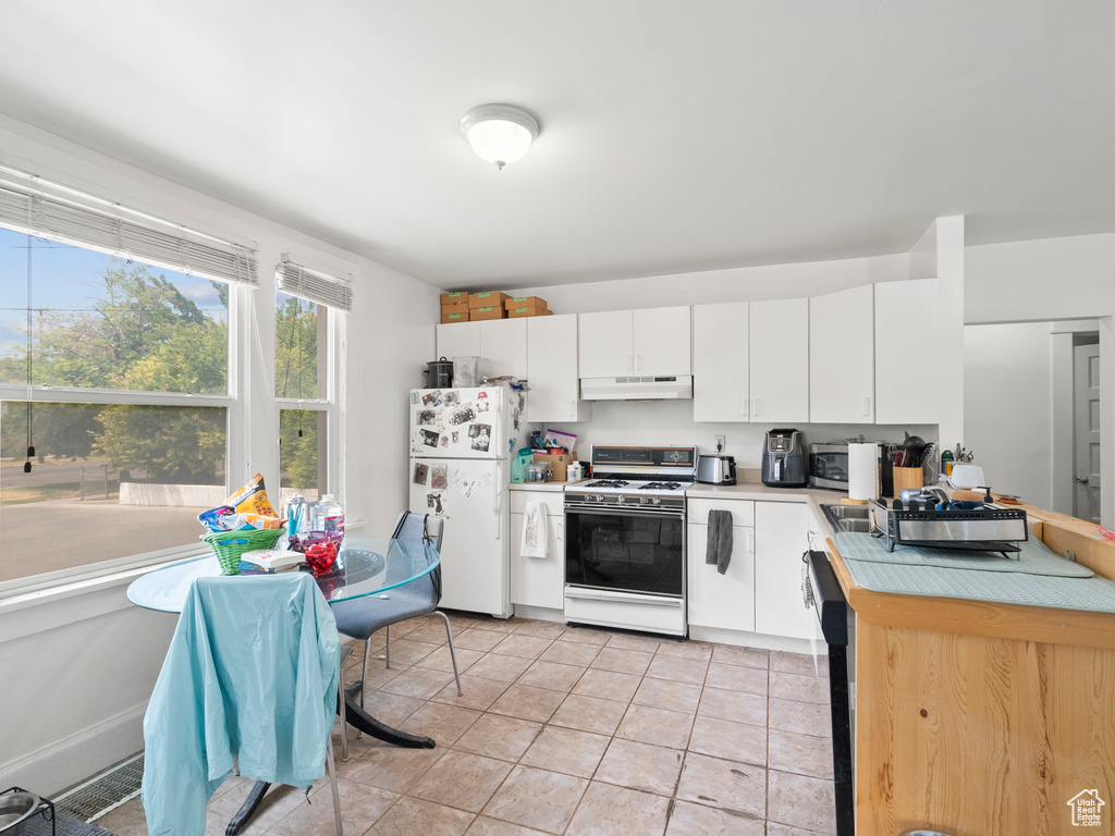 Kitchen featuring white appliances, under cabinet range hood, light countertops, white cabinetry, and light tile patterned floors