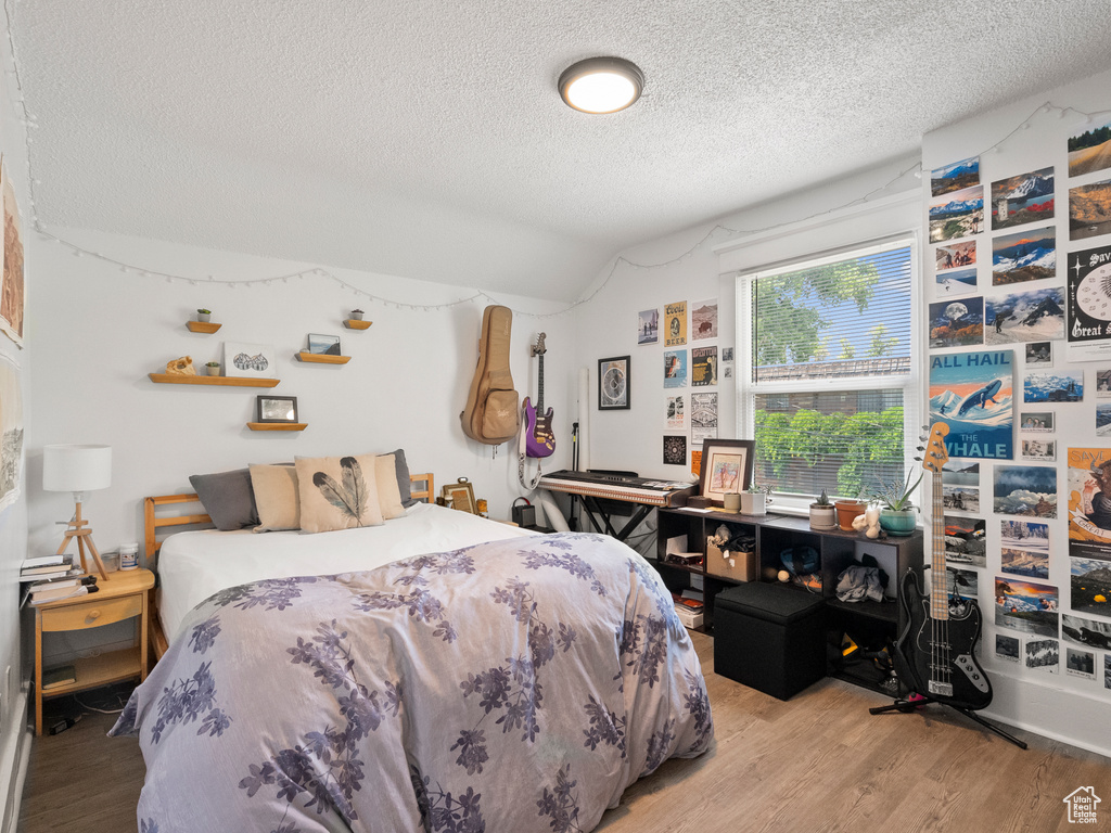 Bedroom featuring a textured ceiling, wood finished floors, and vaulted ceiling
