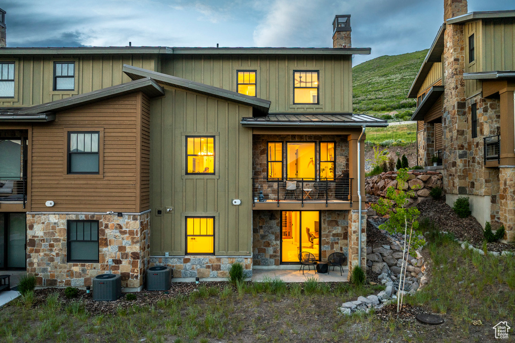 Back of property with stone siding, a chimney, board and batten siding, and a standing seam roof