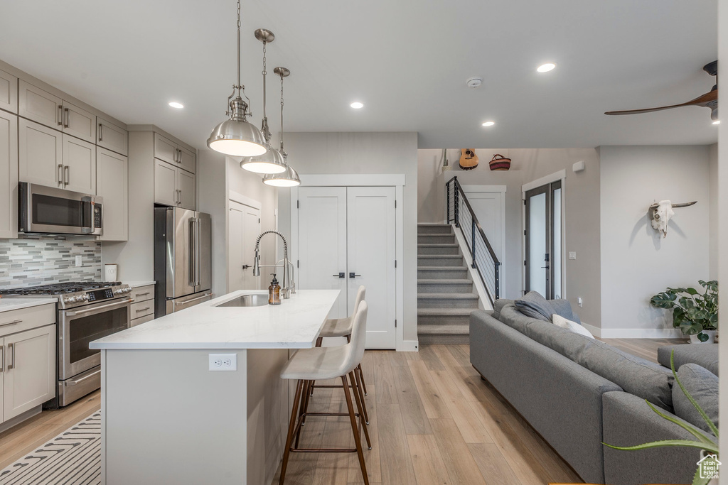 Kitchen featuring stainless steel appliances, light wood finished floors, an island with sink, recessed lighting, and light countertops