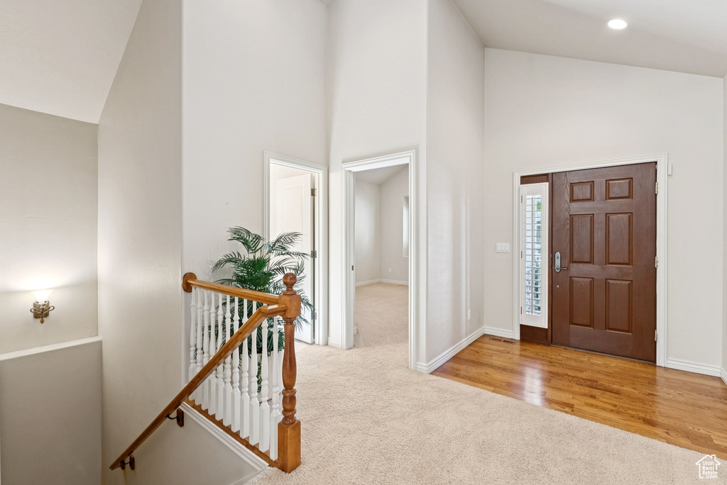 Carpeted foyer featuring high vaulted ceiling and baseboards