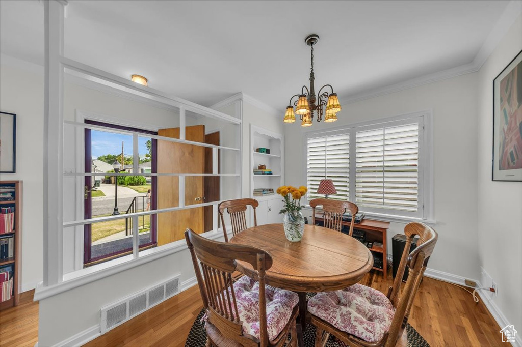 Dining area with a chandelier, light wood-style flooring, and ornamental molding
