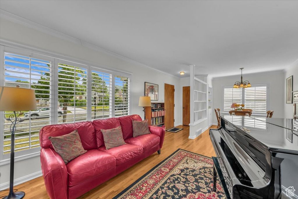 Living area featuring a chandelier, plenty of natural light, light wood-style flooring, and crown molding