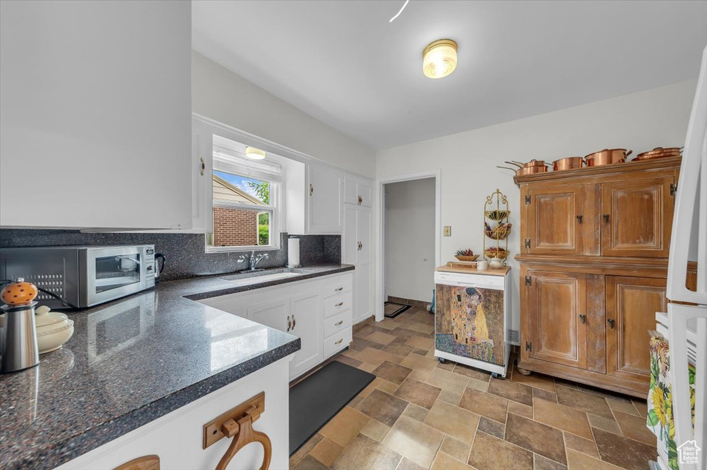 Kitchen with stainless steel microwave, dark countertops, white cabinetry, stone finish flooring, and decorative backsplash
