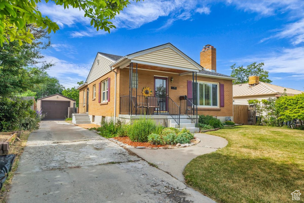 Bungalow featuring an outbuilding, a chimney, concrete driveway, brick siding, and a detached garage