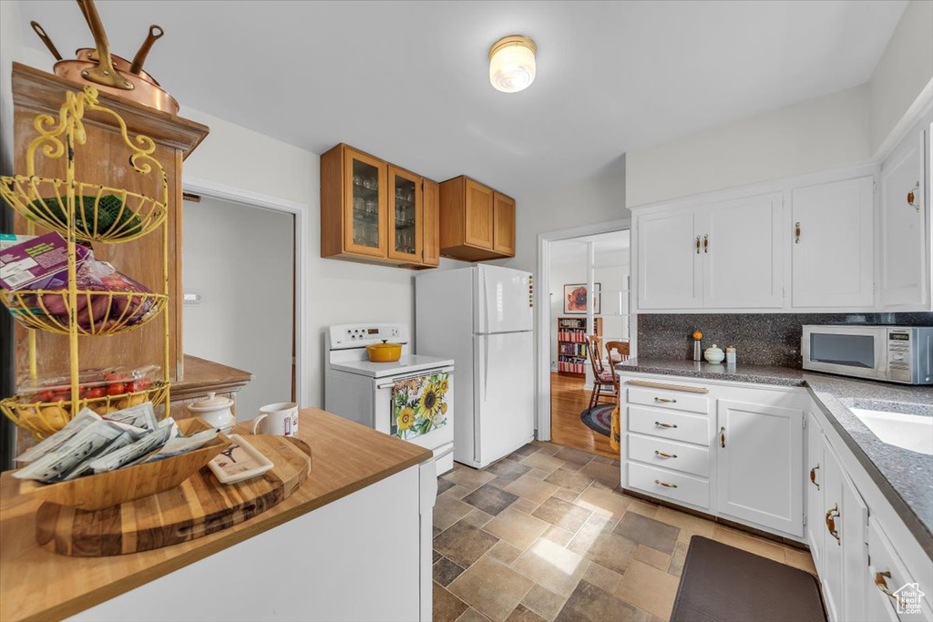 Kitchen with white appliances, stone finish flooring, tasteful backsplash, glass insert cabinets, and white cabinetry