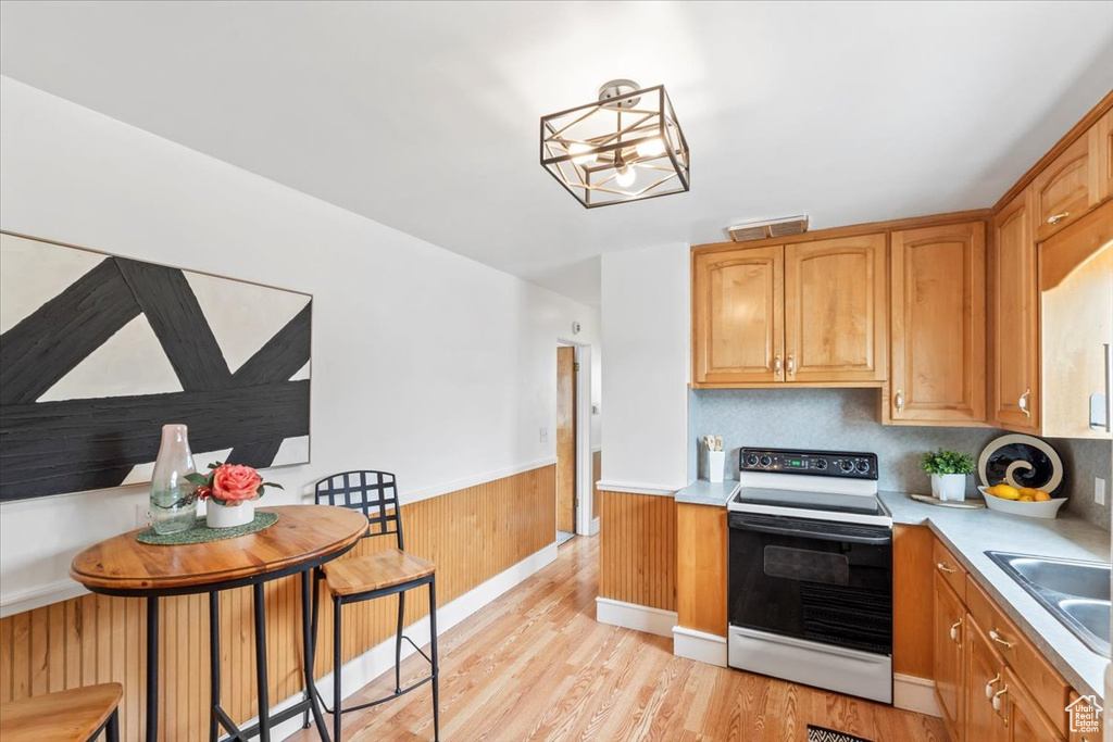 Kitchen with electric range oven, a wainscoted wall, light wood-type flooring, light countertops, and a chandelier