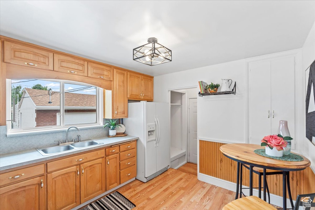 Kitchen featuring white fridge with ice dispenser, light countertops, light wood-style flooring, wainscoting, and backsplash