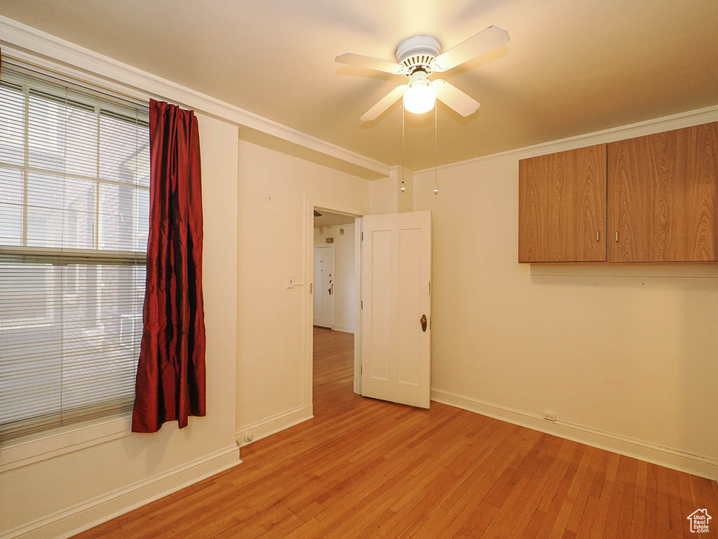 Empty room featuring light wood-type flooring, a ceiling fan, and ornamental molding