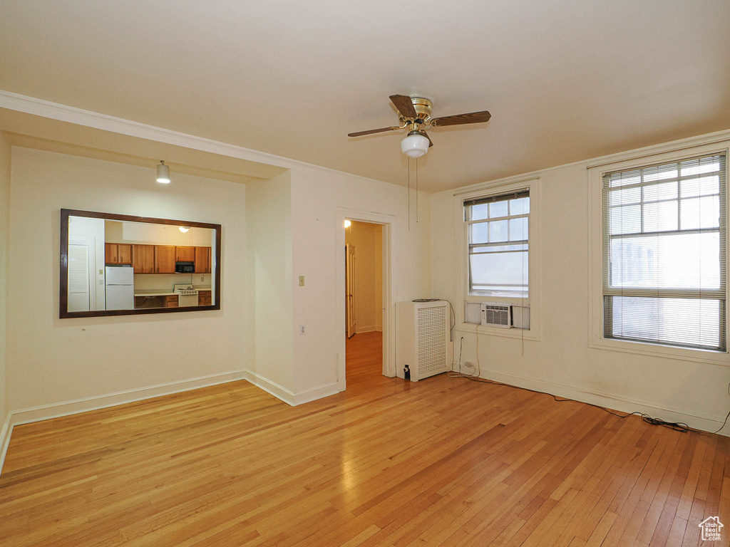 Empty room featuring light wood-style flooring, a ceiling fan, and radiator heating unit