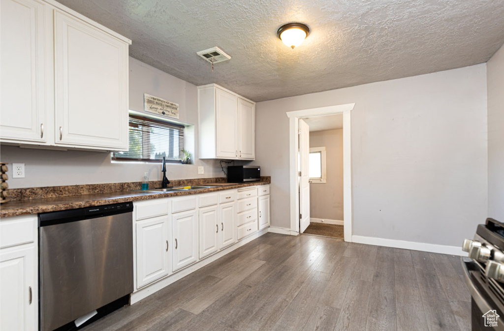 Kitchen with stainless steel appliances, dark wood-type flooring, dark countertops, white cabinets, and a textured ceiling