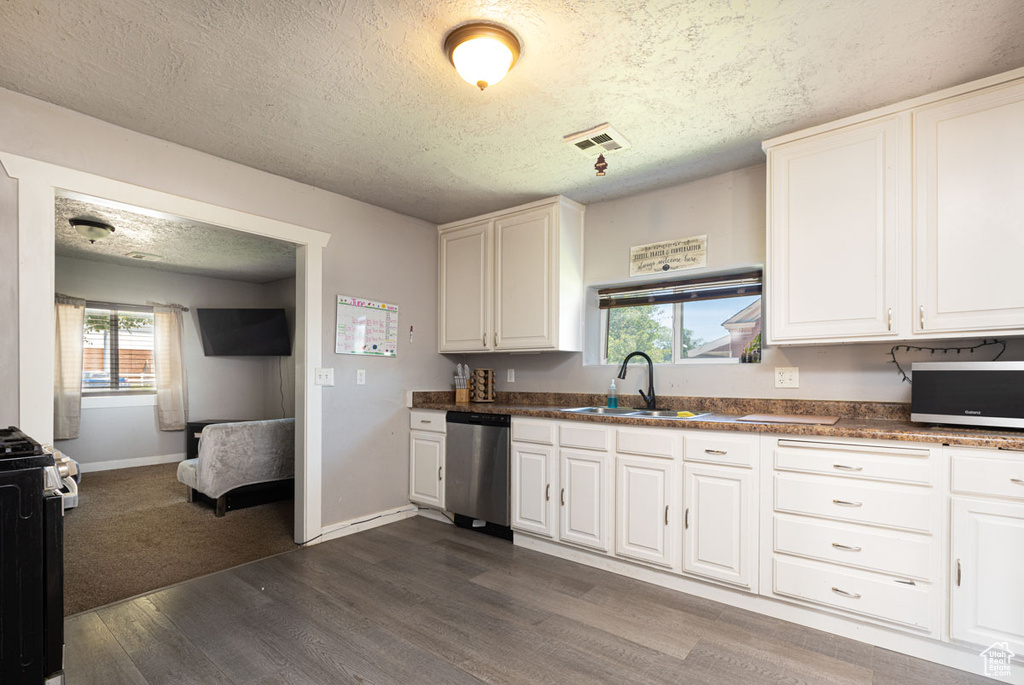 Kitchen with appliances with stainless steel finishes, dark wood-style flooring, a textured ceiling, white cabinets, and dark countertops