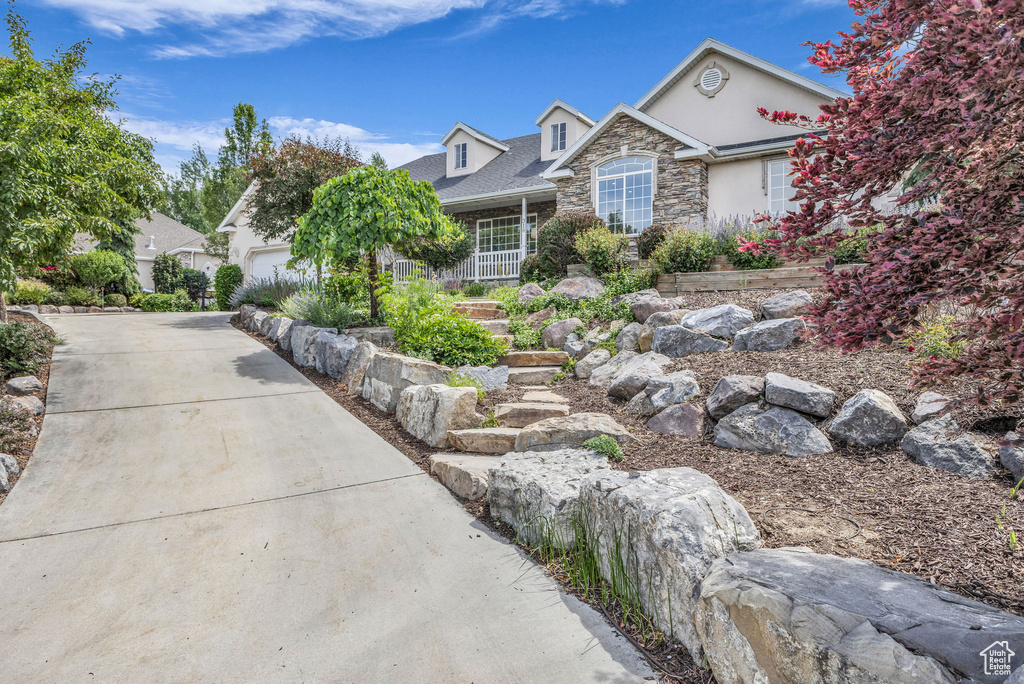 View of front of house featuring stone siding, driveway, an attached garage, and stucco siding