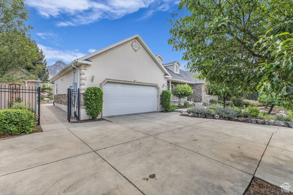 View of home's exterior with stucco siding, concrete driveway, a garage, stone siding, and a gate