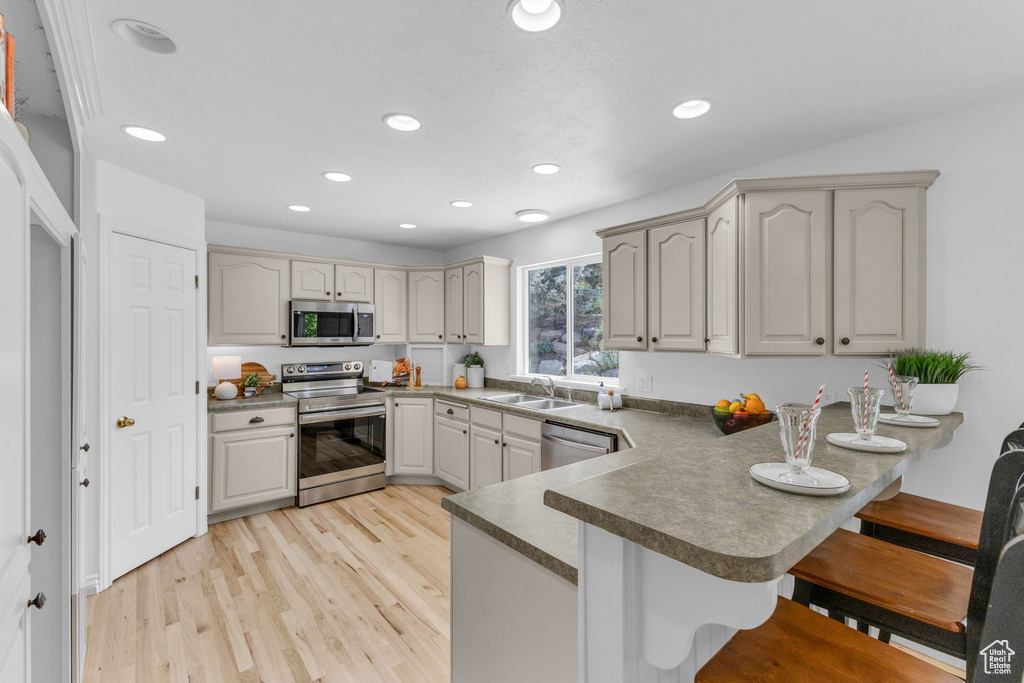 Kitchen featuring appliances with stainless steel finishes, a peninsula, a breakfast bar area, light wood finished floors, and recessed lighting