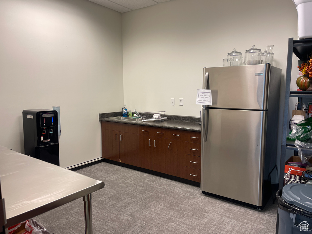 Kitchen with freestanding refrigerator, light carpet, dark countertops, a drop ceiling, and dark brown cabinetry