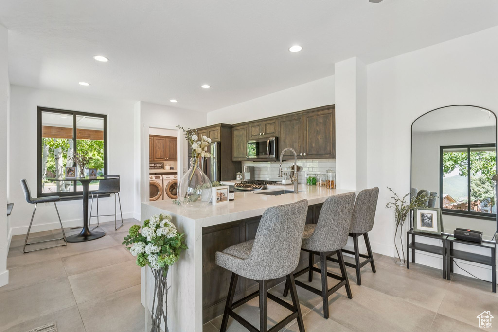 Kitchen with washing machine and clothes dryer, stainless steel microwave, light countertops, a breakfast bar area, and plenty of natural light