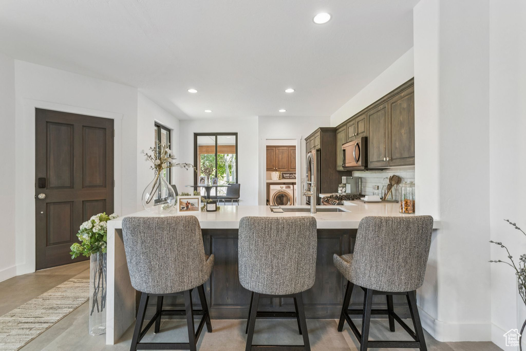 Kitchen with stainless steel microwave, washer / clothes dryer, light countertops, a peninsula, and a breakfast bar