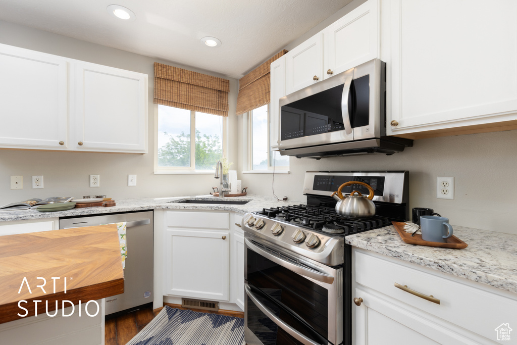 Kitchen with stainless steel appliances, white cabinetry, recessed lighting, dark wood-style floors, and light stone counters