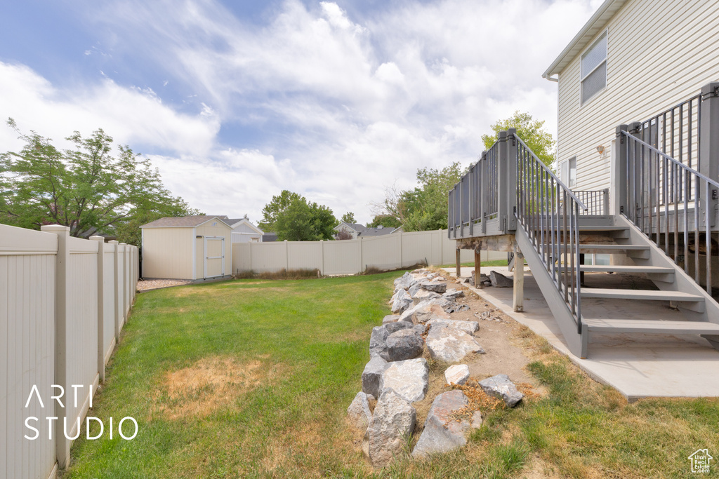 Fenced backyard featuring stairs, a wooden deck, and a storage shed