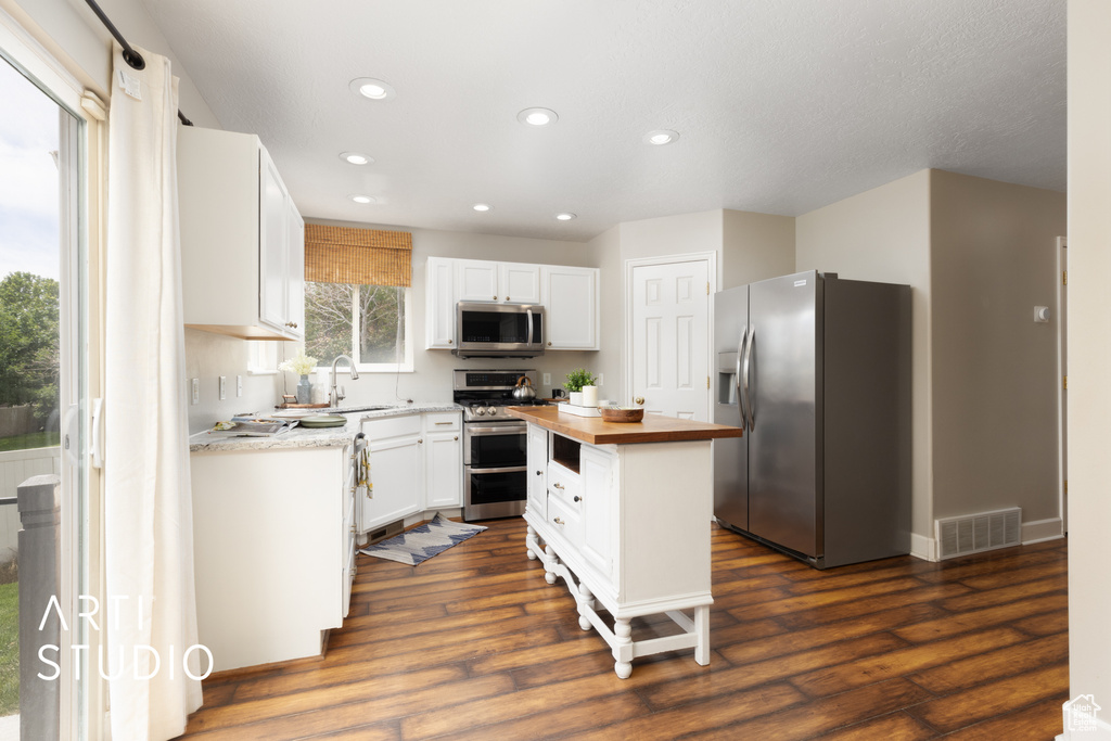 Kitchen featuring appliances with stainless steel finishes, butcher block countertops, recessed lighting, white cabinetry, and dark wood-type flooring