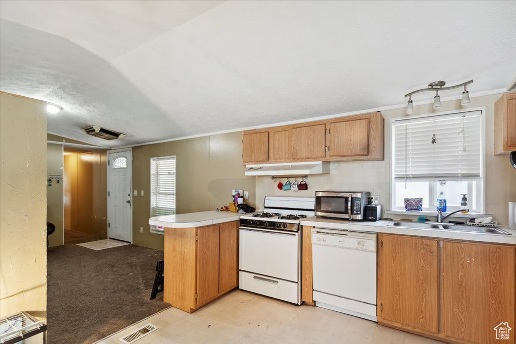 Kitchen featuring white appliances, a peninsula, a sink, light countertops, and under cabinet range hood