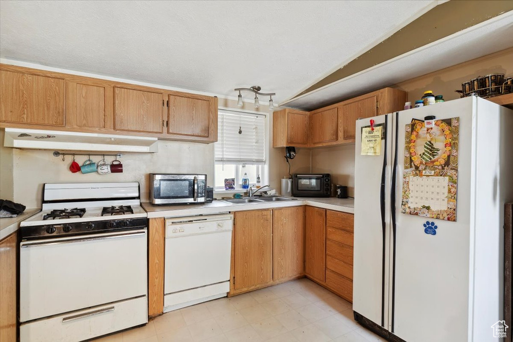 Kitchen with white appliances, under cabinet range hood, vaulted ceiling, a sink, and light countertops